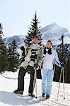 Skiing couple standing, carrying skis on shoulders, on ski slope