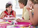 Girl (7-9) mit Geburtstagstorte im Gespräch mit Gästen auf Geburtstagsparty