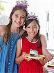 Portrait of two girls (7-9, 10-12) in tiaras, one holding plate with cake, smiling