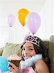 Young girl (7-9) sitting on sofa eating cupcake, close-up