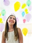 Girl (10-12) in tiara, smiling, looking up at balloons