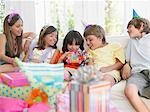 Children (7-12) sitting on sofa, watching one open birthday present