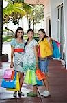 Trois adolescentes (16-17) transportant des sacs à provisions, debout sur la rue, portrait