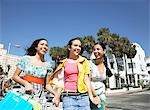 Three teenage girls (16-17) carrying shopping bags, walking on street