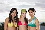 Three teenage girls (16-17) wearing bikinis, standing on beach