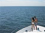 Young couple standing on bow of yacht, looking at seascape, back view
