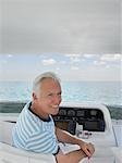 Middle-aged man sitting at helm of yacht, smiling