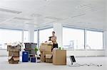 Office worker standing holding potted plant near cartons and equipment on floor of empty office space