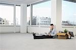 Office worker talking on phone, sitting on floor of empty office space