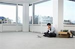 Office worker contemplating phone, sitting on floor of empty office space, side view