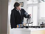 Homme debout dans la cuisine en utilisant le téléphone, verser l'eau dans la cafetière