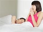 Young couple in bed, man sleeping, woman yawning