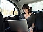 Mid adult woman at back seat of car, using laptop