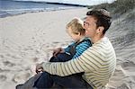 Father embracing daughter (5-6), sitting on beach