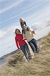 Parents marchant avec fille épaules sur paternel (5-6) sur les dunes, portrait