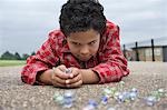 Boy (7-9) playing marbles, lying in playground