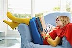 Young boy (7-9) sitting in armchair reading, wearing superhero costume, side view
