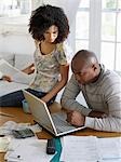 Couple sitting at table, using laptop and holding bills, elevated view