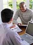 Man sitting at dinning table with financial advisor using laptop, elevated view