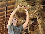 Young man taking photograph of wooden detail of temple