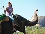 Young man riding elephant, side view, looking over shoulder, mountains in background