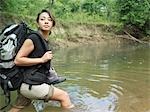 Young woman carrying backpack walking in water, looking over shoulder