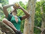 Young woman in tropical forest drinking from coconut, low angle view