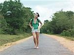 Young woman barefoot, walking rural road, smiling