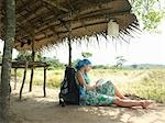 Young woman wearing dress sitting in shade of hut roof