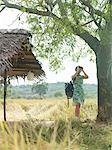 Young woman looking through binoculars by thatched roof