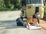 Young woman sitting on road reading map, motor scooter in background