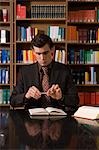 Man wearing suit holding pen over book at desk in library