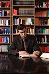 Man wearing suit writing at desk in library