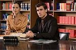 Young man and woman studying at desk in library, portrait