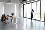 Man using mobile phone, leaning against window in empty office building