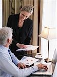 Business man using laptop, business woman sitting on desk holding documents, elevated view