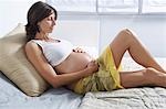 Pregnant woman holding stomach on bed in bedroom
