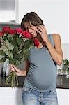 Femme enceinte à l'aide de téléphone mobile tout en gardant des roses dans la cuisine