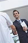 Male estate agent shaking hands with customer, indoors
