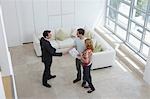 Real estate agent with couple in new home, man shaking hand, elevated view