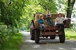 Three children (5-9) sitting on trailer on country lane