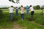 Parents with three children (5-9) standing on fence in countryside