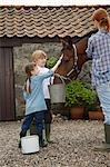 Mother and children (5-6, 7-9) feeding horse outside stable