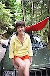 Woman sitting on car bonnet in forest