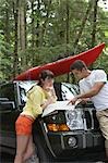 Couple observing map on car bonnet in forest