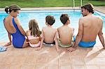 Family with three children (6-11) sitting by pool, back view