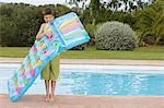 Boy (10-12) blowing up air mattress by pool