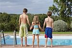 Deux garçons et filles (6-11) debout sur le bord de la piscine, vue arrière