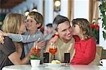 Parents and children (7-9) with drinks, embracing at restaurant