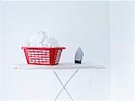 Iron and laundry basket on ironing board against white wall